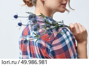 A woman is holding fresh blue eryngium flowers on her shoulder against a gray background. Happy Mother’s Day. Young girl with flowers eryngium. Стоковое фото, агентство Ingram Publishing / Фотобанк Лори