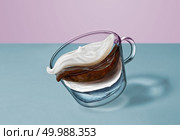 Creative composition of coffee beverage - flying layers of water, coffee, milk, creamy foam in a glass cup moving above the surface of the blue table.. Separate flying layers of coffee, milk, water, milk foam in the coffee drink in a transparent cup on a duotone background. Стоковое фото, агентство Ingram Publishing / Фотобанк Лори