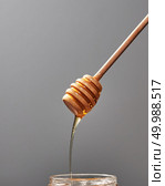 Dripping sweet honey into a jar with fresh organic syrup on a gray background, place for text. Jewish rosh hashanah holiday concept.. Close up of wooden stick with dripping sweet natural honey on a gray background, traditional useful sweetness. Стоковое фото, агентство Ingram Publishing / Фотобанк Лори