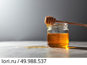 Fragrant natural organic honey dripping from wooden dipper into a gray kitchen marble table, place for text. Rosh hashanah jewish New Year healthy holiday concept.. Wooden honey spoon above on a glass jar full natural organic syrup in a glass pot on a gray stone table. Traditional healthy sweetness. Стоковое фото, агентство Ingram Publishing / Фотобанк Лори