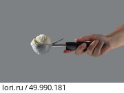 A female hand holds delicious dairy dessert cold white vanilla in a metal spoon for ice cream on a gray background. Summer consept with copy space.. A ball of homemade vanilla white ice cream in a metal scoop holds a woman’s hand on a gray background. Copy space. Стоковое фото, агентство Ingram Publishing / Фотобанк Лори