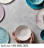 Vintage painted plates dishes on gray concrete table with free space ror text in the center. Girl hold handcraft bowl in her hand. Flat lay.. Colorful porceain vintage handmade dishes on a marble table with copyspace. Woman hands take a white ceramic bowl. Top view. Стоковое фото, агентство Ingram Publishing / Фотобанк Лори