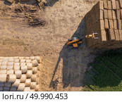 Aerial view agricultural machinery tractor stacks bales of hay in the field. Photo from drone. Autumn harvest. Top view. Aerial view from drone large stacks of dry hay bales in the field. Tractor folds bales of hay on a sunny day. Top view. Стоковое фото, агентство Ingram Publishing / Фотобанк Лори