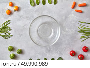 Empty glass plate and fresh vegetables on a gray concrete background, the first stage of salad cooking, a photo from a series of turn-based salad cooking. Top view, flat lay. Vegetables, ingredients for cooking salad. Стоковое фото, агентство Ingram Publishing / Фотобанк Лори