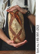 Close up hands man holding an oval fresh bread on a background. Hands of man holding oval bread. Стоковое фото, агентство Ingram Publishing / Фотобанк Лори