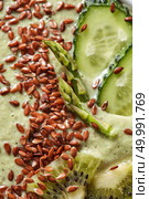 Vegetarian food smoothies from green organic vegetables with flax seeds in a white bowl, macro natural green background. Top view.. Top view of natural green background - a green smoothie from avacado, cucumber, kiwi, asparagus with flax seeds. Стоковое фото, агентство Ingram Publishing / Фотобанк Лори