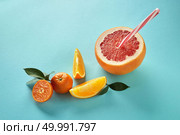 Tropical exotic citrus fruits half a grapefruit, tangerines, orange slices with a plastic straw for juice on a blue paper background. Exotic citrus fruits with green leaves and plastic straw for juice on a blue paper background. Стоковое фото, агентство Ingram Publishing / Фотобанк Лори