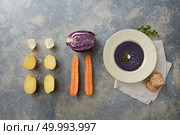 Delicious vegan healthy soup represented near its ingredients: carrot, potato, onion, cabbage. Vegan soup in white plate on table. Some sliced buns near it. Miso soup concept.. Vegan soup over grey. Стоковое фото, агентство Ingram Publishing / Фотобанк Лори