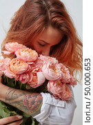 pretty red-haired girl with a tattoo on her arm holding and smell a bouquet of pink roses, valentine’s day, mother’s day. pretty girl holding a bouquet of pink roses. Стоковое фото, агентство Ingram Publishing / Фотобанк Лори