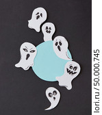 Greeting card, creative application with handmade paper terrible spirits smiling and laughing ghosts on a black background, place under text. Halloween concept. Flat lay.. Halloween party round frame with habdcrafted laughing flying scary ghosts, spirits, around it on a black background. Стоковое фото, агентство Ingram Publishing / Фотобанк Лори