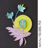 Decorative handcraft composition from paper with flowers, leaf and skull on a yellow round frame on black paper background, copy space. Calaveras attribute of the Mexican holiday of Calaca. Flat lay. Greeting card with Calaveras skull, decorated paper flowers calendula, leaf and creative on a yellow frame on a black paper. Стоковое фото, агентство Ingram Publishing / Фотобанк Лори