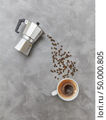 Coffee beans pour in a cap with drink from a metal coffee maker on a gray background with copy space. Concept of morning breakfast. Flat lay. Italian coffee maker and fresh coffee beans coffee beans in the form of a drink stream on a gray stone background. Top view. Стоковое фото, агентство Ingram Publishing / Фотобанк Лори