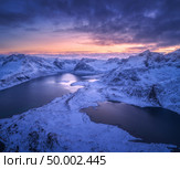 Aerial view of snowy mountains, sea, colorful cloudy sky at night in Lofoten islands, Norway. Winter landscape with snow covered rocks and seacoast and sunset sky. Top view of Norwegian Fjords at dusk. Стоковое фото, агентство Ingram Publishing / Фотобанк Лори