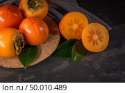 Ripe persimmon fruits in a cork plate on dark kitchen counter top. Стоковое фото, агентство Ingram Publishing / Фотобанк Лори