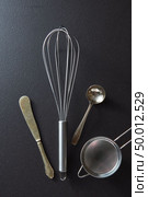 Old knife, whisk, spoon and sieve presented on a black concrete background with space for text. Top view. Set of kitchen tools knife, whisk, sieve and spoon on black concrete background with copy space. Top view. Стоковое фото, агентство Ingram Publishing / Фотобанк Лори
