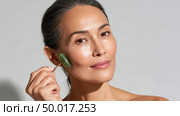 Woman using jade roller massaging face for skin care routine. Стоковое AI-изображение, AI-художник Юрий Поздников / Фотобанк Лори