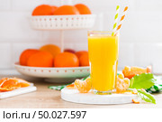 Tangerine orange juice in glass and fresh fruits with leaves on white wooden kitchen background closeup. Healthy and tasty refreshing summer beverage. Стоковое фото, агентство Ingram Publishing / Фотобанк Лори