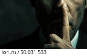 A close view of a mans face, focusing on his hand gesture asking for silence, in a dark setting. Стоковое AI-изображение, AI-художник Данила Большаков / Фотобанк Лори