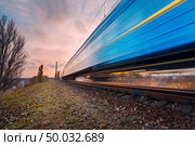 High speed blue passenger train on railroad track in motion at sunset. Blurred commuter train. Railway station with cloudy sky. Railroad travel, railway tourism. Industrial landscape at dusk. Стоковое фото, агентство Ingram Publishing / Фотобанк Лори