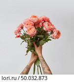 Beautiful bouquet of fresh roses in woman’s hands with tatoo in a color of the year 2019 Living Coral Pantone on a gray background with copy space. Top view.. Girl’s hands with tattoo hold a bouquet of fresh roses in a color of the year 2019 Living Coral Pantone on a gray background. Стоковое фото, агентство Ingram Publishing / Фотобанк Лори