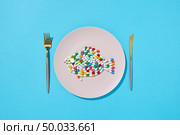 Many different pills and supplements as food on round white plate with fork and knife. Diet pills and supplements for dieting concept. Top view.. Colorful capsules and pills in the form of fish on a plate with fork and knife on a blue background, copy space. Top view. Стоковое фото, агентство Ingram Publishing / Фотобанк Лори