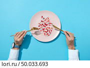 Fish from colorful pills and tablets on a white plate, girl’s hands with watch on a blue background with shadows, copy space. The negative effect of pills on cardiovascular diseases. Top view.. Vitamin pills on a white plate in a shape of fish with spoon and fork in a girl’s hands on a blue background, copy space. The negative effect of pills on cardiovascular diseases. Стоковое фото, агентство Ingram Publishing / Фотобанк Лори