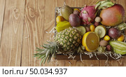 Box with assortment of freshly picked natural exotic fruits -ananas, passion fruit, mango on a wood shaving on a wooden background. Panoramic slow motion, 4K UHD video, 3840, 2160p. Top view.. Panoramic video top view on a box with variety fresh natural organic exotic fruits on a wooden background. Slow motion, 4K UHD video, 3840, 2160p. Стоковое фото, агентство Ingram Publishing / Фотобанк Лори