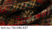 A small orange tabby kitten with large eyes peeks out from under a colorful knitted blanket. The scene conveys warmth and coziness. Стоковое AI-изображение, AI-художник Светлана Леуто / Фотобанк Лори