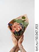 Spring wonderful fresh roses, eryngium and green leaves as a greeting bunch in a girl’s hands with tattoo on a light background. Place for text. Gift for Mother’s Day.. Woman’s hands hold colourful blossoming flower bouquet of fresh roses living coral color on a gray background. Copy space. Mother’s and Woman’s Day. Стоковое фото, агентство Ingram Publishing / Фотобанк Лори