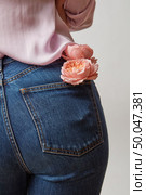 Beautiful female butt in jeans with fresh roses of coral living color in a back pocket on a light gray background. Place for text.. Woman wearing of jean pants and pink shirt from back with fresh flowers in a pocket on a gray background, copy space. Стоковое фото, агентство Ingram Publishing / Фотобанк Лори