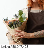 Wonderful summer fresh roses, eryngium and green leaves as a greeting bouquet in a female’s hand with tattoo on a white background. Place for text. Gift for Mother’s Day.. Young girl with ginger hair hold beautiful bunch with fresh natural flowers and leaves on a light background, copy space. Holiday card. Стоковое фото, агентство Ingram Publishing / Фотобанк Лори