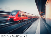 Beautiful railway station with modern high speed red commuter train with motion blur effect at sunset in Nuremberg, Germany. Railroad. Vintage toning. Railroad travel background, tourism. Industrial. Стоковое фото, агентство Ingram Publishing / Фотобанк Лори