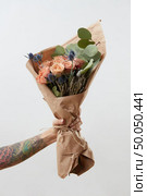 Nice flowers living coral roses and eryngium as a congratulate bouquet in girl’s hand with tattoo, copy space. Post card for Mother’s Day.. Female hand shows bouquet with rose flowers on gray background. Gift for Mother or Woman’s Day. Стоковое фото, агентство Ingram Publishing / Фотобанк Лори
