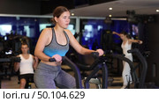 Determined young girl training with air bike in fitness hall during full-body workout. Стоковое видео, видеограф Яков Филимонов / Фотобанк Лори