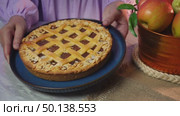 Woman presenting freshly baked apple pie with basket of apples on rustic table setting. Стоковое видео, видеограф Zakharova Natasha / Фотобанк Лори