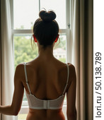 A stunning woman stands gracefully at her window, showcasing a chic lingerie design. Soft light filters through, highlighting her back while she gazes outside, lost in thought Generative AI. Стоковое AI-изображение, AI-художник Юлия Петровская / Фотобанк Лори