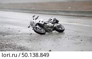 Motorcycle lies on wet road after accident in rainy conditions. Стоковое AI-изображение, AI-художник Katsiaryna Repich / Фотобанк Лори