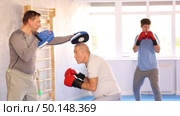 Positive interested elderly man in boxing gloves punching on mitts in hands of adult son during joint workout in training room. Стоковое видео, видеограф Яков Филимонов / Фотобанк Лори