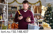 Interested man chooses wine and champagne in a supermarket with a Christmas tree in the background. The buyer chooses alcohol for the holiday. Стоковое видео, видеограф Яков Филимонов / Фотобанк Лори