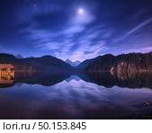 Colorful night landscape with lake, mountains, forest, stars, full moon, purple sky and clouds reflected in water. Spring night in Alpsee lake in Germany. Panoramic photo. Nature background. Стоковое фото, агентство Ingram Publishing / Фотобанк Лори