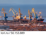 Sea commercial port at night in Mariupol, Ukraine. Industrial view. Cargo freight ship with working cranes bridge in sea port at twilight. Cargo port, logistic. Стоковое фото, агентство Ingram Publishing / Фотобанк Лори