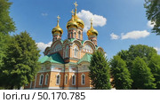 A majestic white Orthodox church with golden domes stands in a park with colorful autumn trees under a blue sky with clouds. Стоковое AI-видео, аниматор Sergey Grishin / Фотобанк Лори