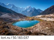 Small lake with blue water and sky reflection against beautiful snow covered mountains at sunny day in autumn. Landscape with lake, snowy rocks, hills, stones at sunrise. Himalayan mountains in Nepal. Стоковое фото, агентство Ingram Publishing / Фотобанк Лори
