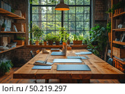 A modern, cozy office or coworking space with an emphasis on eco-friendliness and natural light. The interior is designed in a loft style with brick walls, wooden furniture and lots of indoor plants. A large panoramic window lets in soft daylight, filling the space with warmth and harmony. Laptops, documents, a cup of coffee and work materials are laid out on a wooden table - creating an atmosphere of productive but comfortable work. Suitable for themes of remote work, eco-design, modern architecture, green offices and creative spaces. Стоковое AI-изображение, AI-художник Анна Кривицкая / Фотобанк Лори