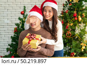 beautiful asian girl give surprise christmas gift to her boyfriend in Christmas holiday season greeting. Стоковое фото, агентство Ingram Publishing / Фотобанк Лори
