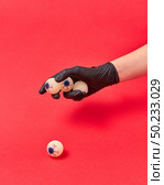 Woman hand in a black glove holds human eyeballs on a red background, copy space. Halloween simbol.. Woman hand in black glove with human eyeballs. Стоковое фото, агентство Ingram Publishing / Фотобанк Лори