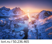 Aerial view of snowy mountains, sea, purple sky at sunset in Lofoten islands, Norway. Winter colorful landscape with snow covered rocks, frosty seacoast, road and village. Top view of Norwegian Fjords. Стоковое фото, агентство Ingram Publishing / Фотобанк Лори