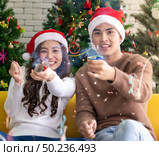 Young asian adult teenager couple celebrateing christmas holiday together with Firecrackers in living room with christmas tree decoration. Стоковое фото, агентство Ingram Publishing / Фотобанк Лори