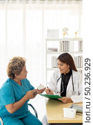 Asian female doctor talking prescribing pills to old senior elderly patient in examination room of clinic hospital. Стоковое фото, агентство Ingram Publishing / Фотобанк Лори