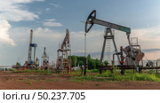 Oil production at the field using two rocking machines. In the background is a drilling rig and equipment for drilling wells. Summer. Beautiful sky and nature. Стоковое фото, фотограф Владимир Ендовицкий / Фотобанк Лори